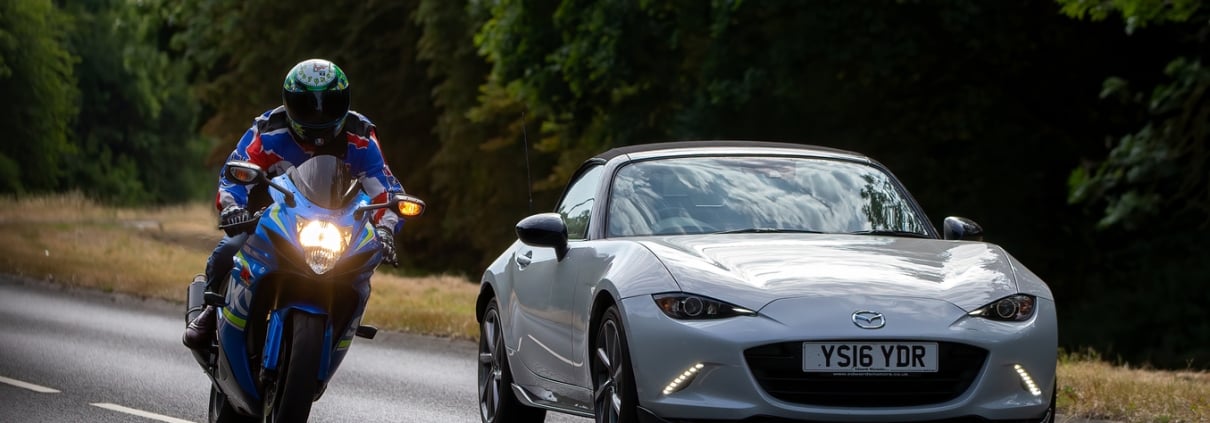 Man riding a Suzuki motorcycle overtakes a Mazda MX5 car on the A5