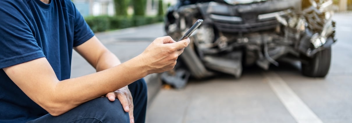 Man calling with phone to his insurance agent after traffic accident with a background of the crashed car, Car insurance an non-life insurance concept.