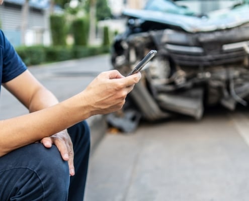 Man calling with phone to his insurance agent after traffic accident with a background of the crashed car, Car insurance an non-life insurance concept.