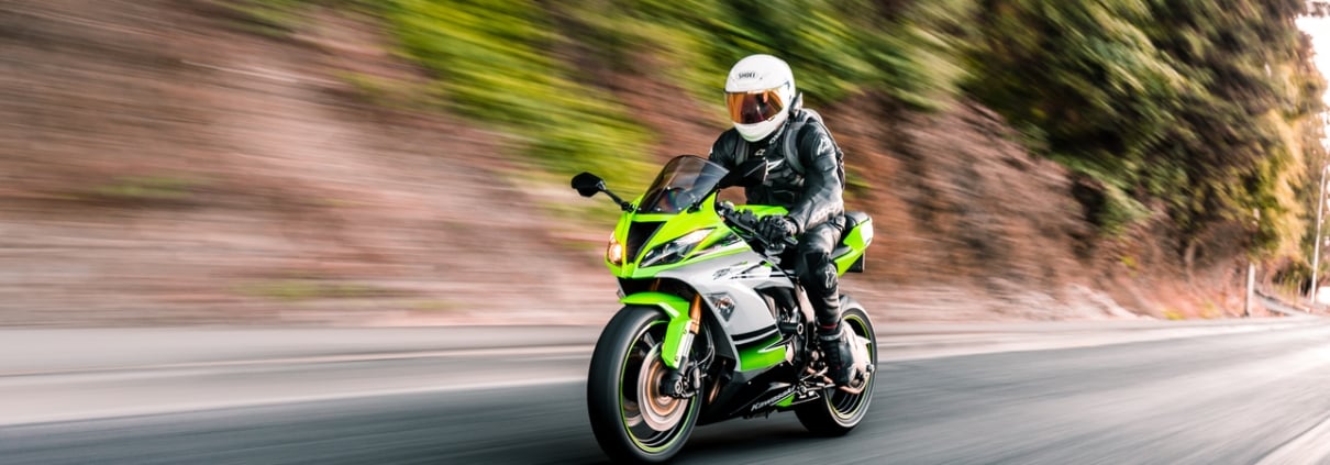 Green Kawasaki motorcycle being driven on the streets with trees in the background