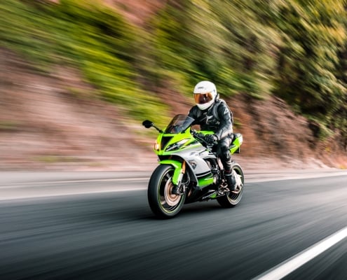 Green Kawasaki motorcycle being driven on the streets with trees in the background