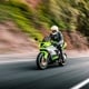 Green Kawasaki motorcycle being driven on the streets with trees in the background