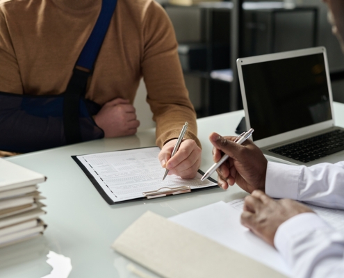 Close up of man filling in medical insurance form, injured hand in sling in background, copy space