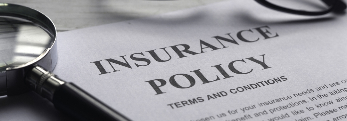 Selective focus of magnifying glass,glasses and Insurance Policy letter on a white wooden background.