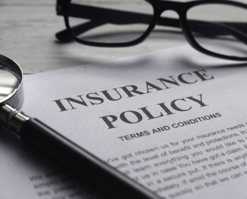 Selective focus of magnifying glass,glasses and Insurance Policy letter on a white wooden background.