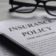 Selective focus of magnifying glass,glasses and Insurance Policy letter on a white wooden background.